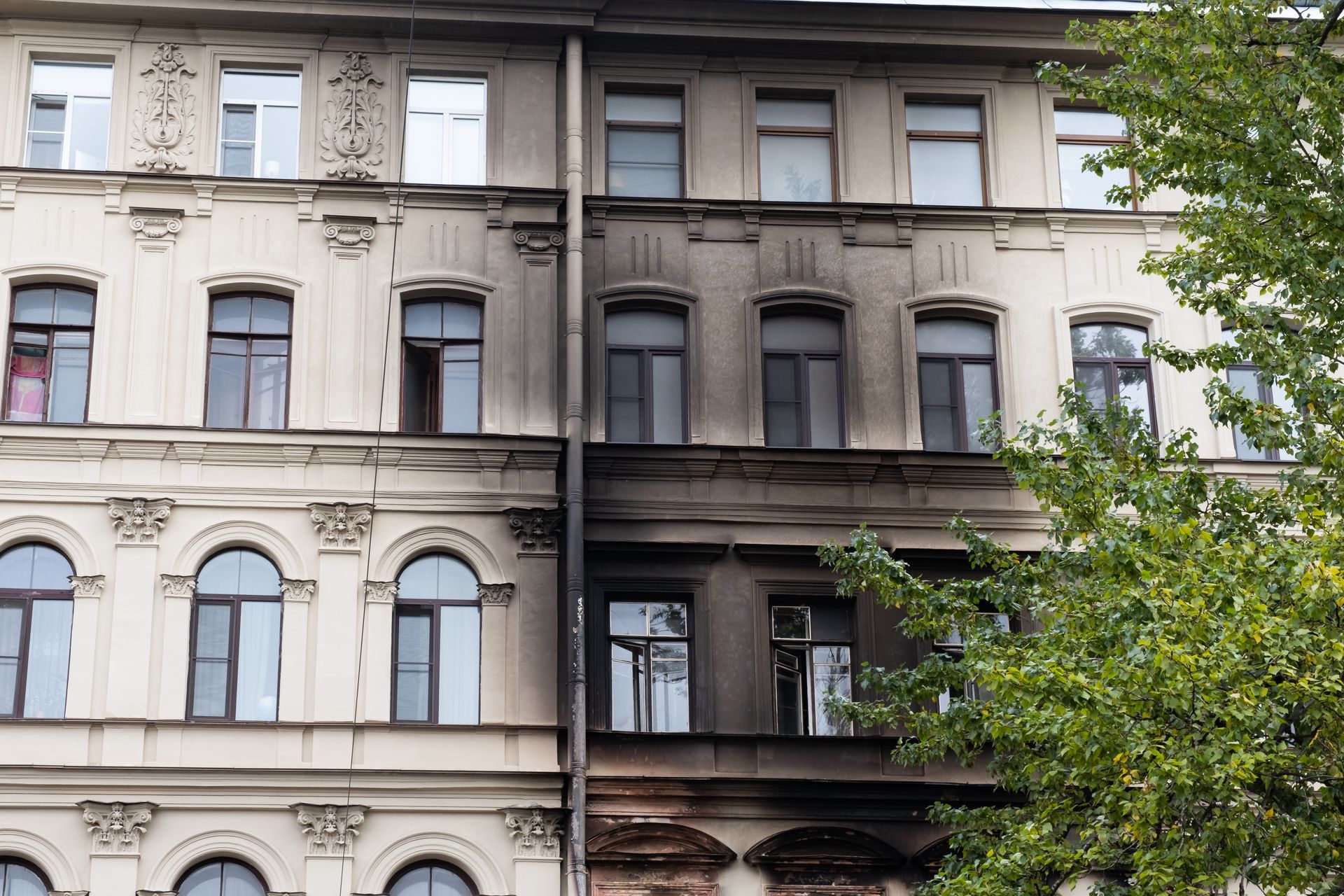 La façade d'un immeuble présente un contraste saisissant entre un côté propre et clair et un côté carbonisé.