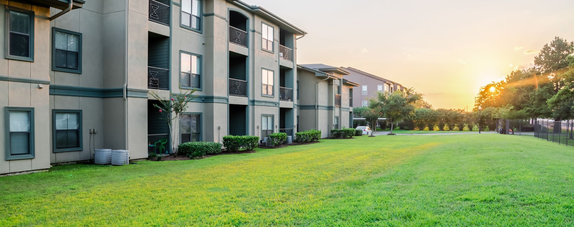 Extérieur d'un immeuble d'appartements moderne à étages, avec des murs beiges, des balcons sombres et une pelouse.
