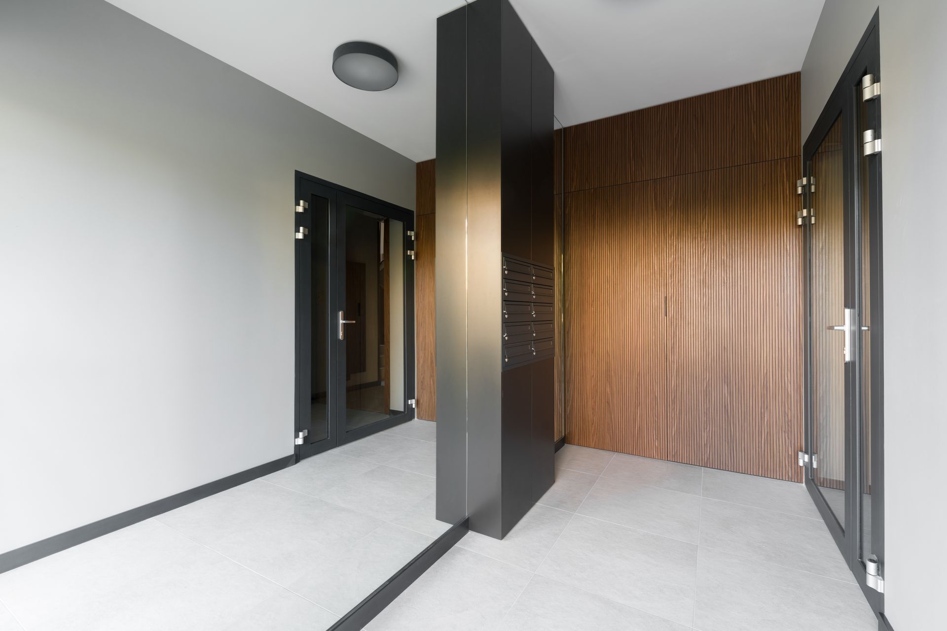 Entrée moderne avec murs blancs, colonne centrale gris foncé, mur d'accent en lattes de bois et portes vitrées.