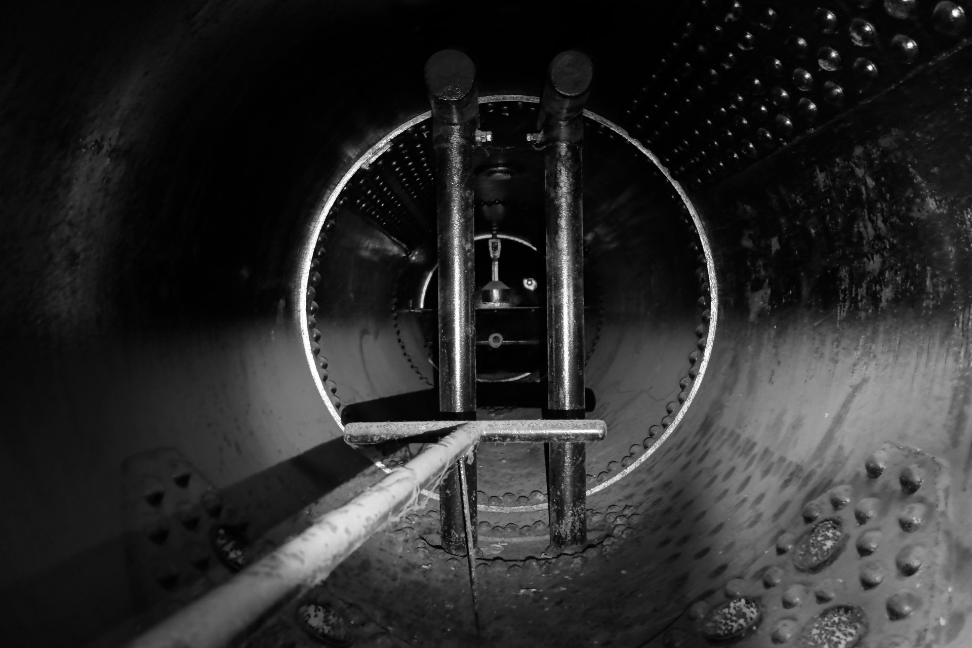 Vue intérieure d'une grande structure cylindrique métallique sombre, avec des tuyaux verticaux et une tige au premier plan.