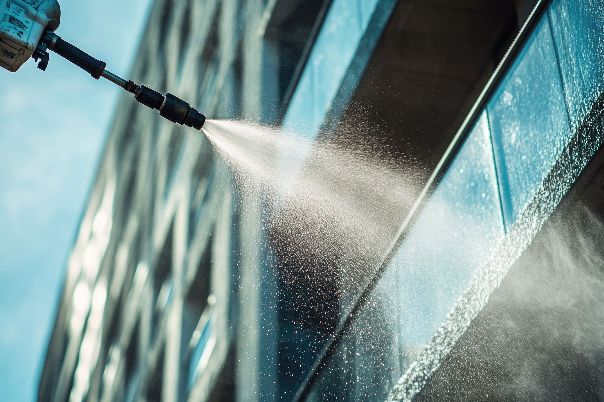 Un nettoyeur à haute pression projette un jet d'eau contre la rambarde en verre et la façade d'un bâtiment moderne.