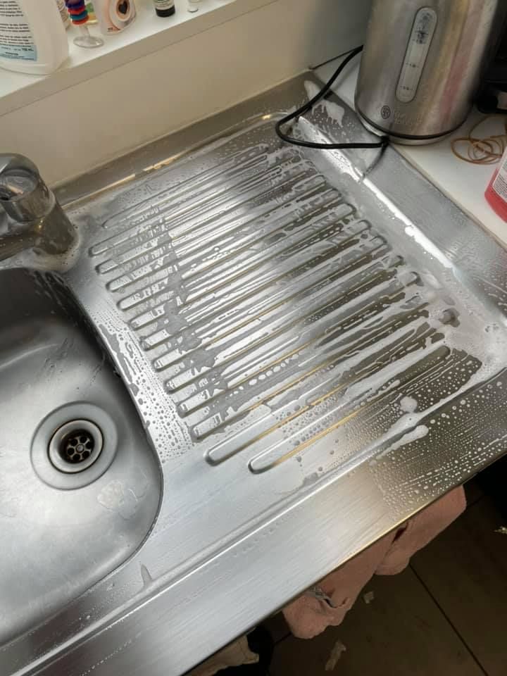 Un égouttoir d'évier en acier inoxydable avec des résidus d'eau savonneuse, à côté d'une bouilloire sur un comptoir.