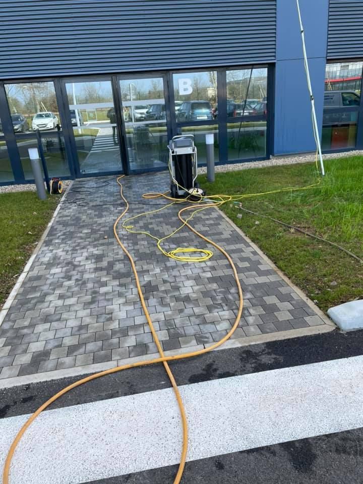 Une machine de nettoyage de vitres portable avec des tuyaux sur une allée pavée à l'extérieur d'une entrée de bâtiment.