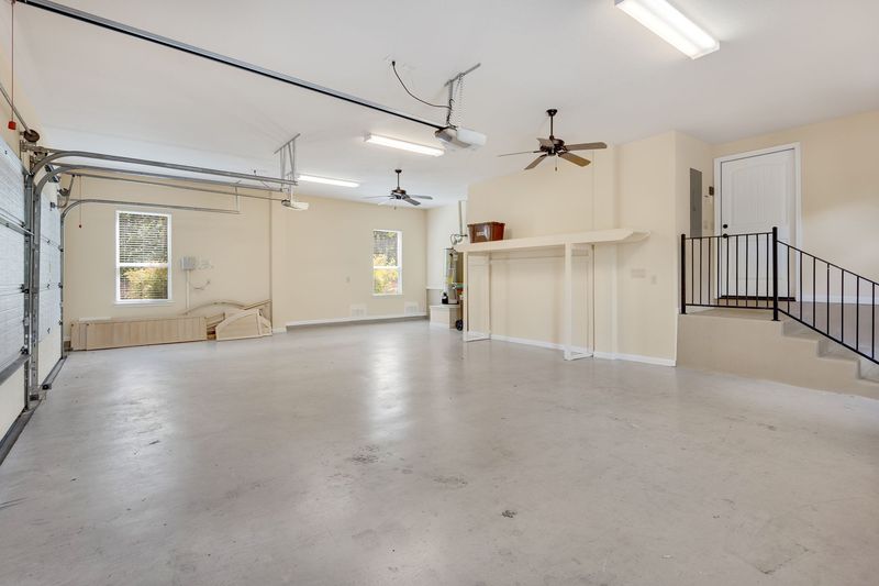 Un vaste espace vide, aux murs beiges, au sol en béton gris, avec des ventilateurs de plafond et un escalier.