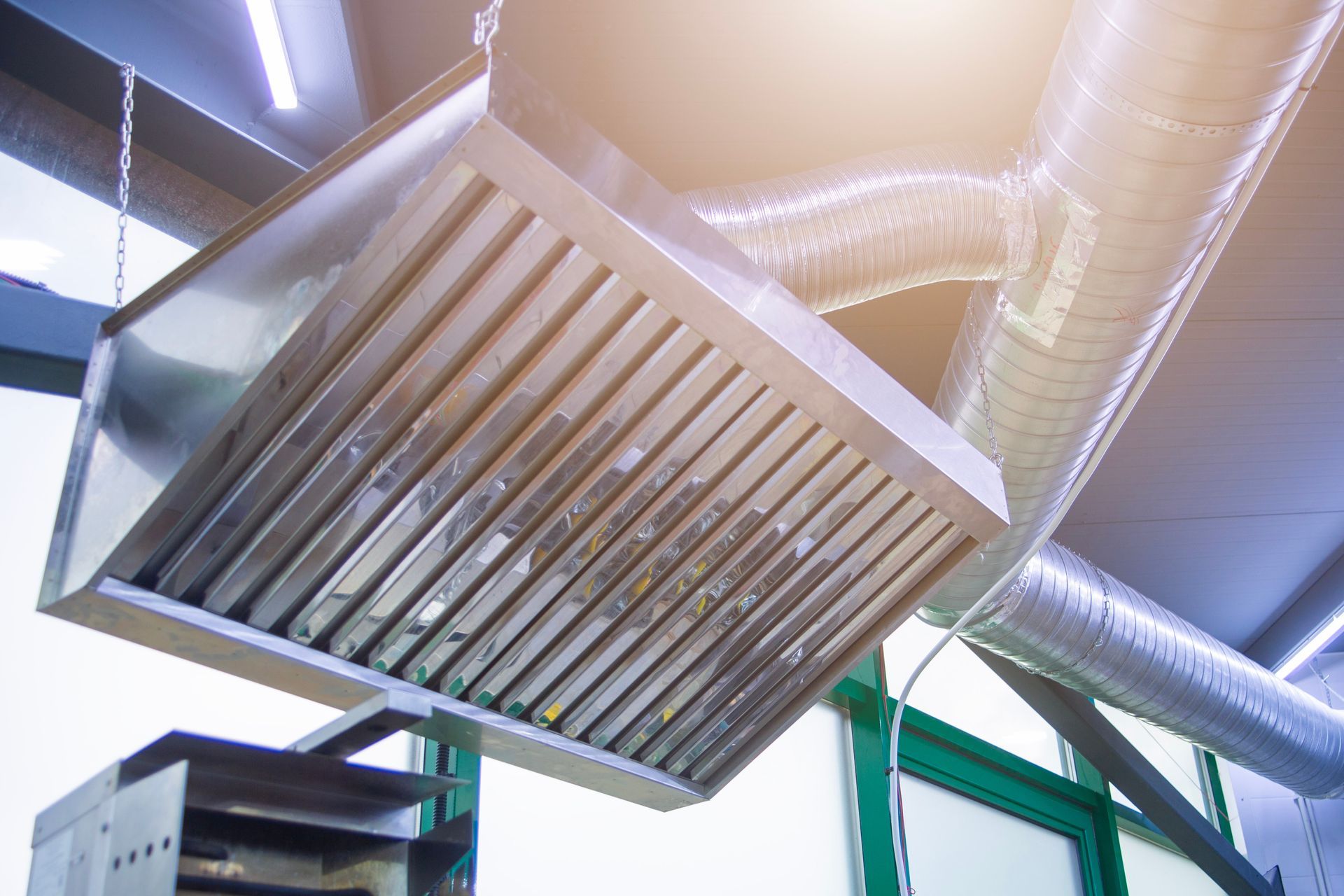 Une hotte aspirante de cuisine commerciale en acier inoxydable suspendue par des chaînes au-dessus d'une plaque de cuisson.