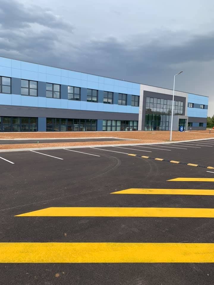 Un bâtiment commercial moderne de deux étages, revêtu de panneaux bleu clair et gris et stationnement pavé aux marquages jaunes.