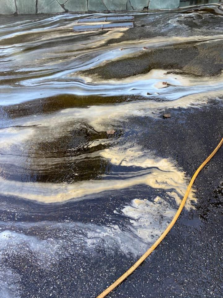 Un tuyau jaune repose sur l'asphalte mouillé, laissant apparaître des motifs tourbillonnants d'eau et de fioul.