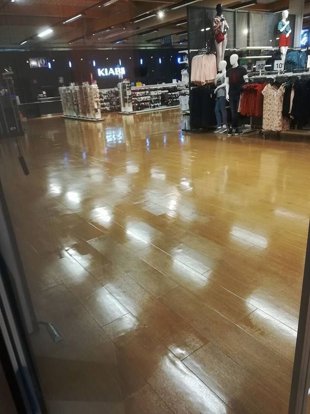 Vue intérieure d'un magasin de vêtements avec un parquet vitrifié et des portants à vêtements sous un éclairage intense.