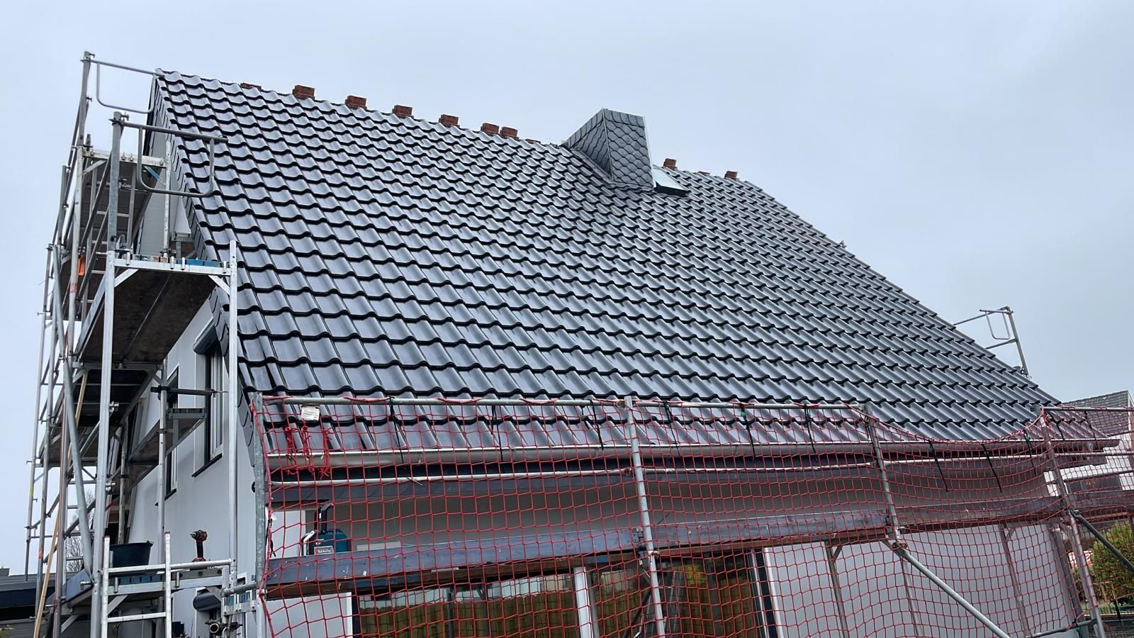 Ein Haus mit Ziegeldach wird gebaut, drumherum ist ein Gerüst.