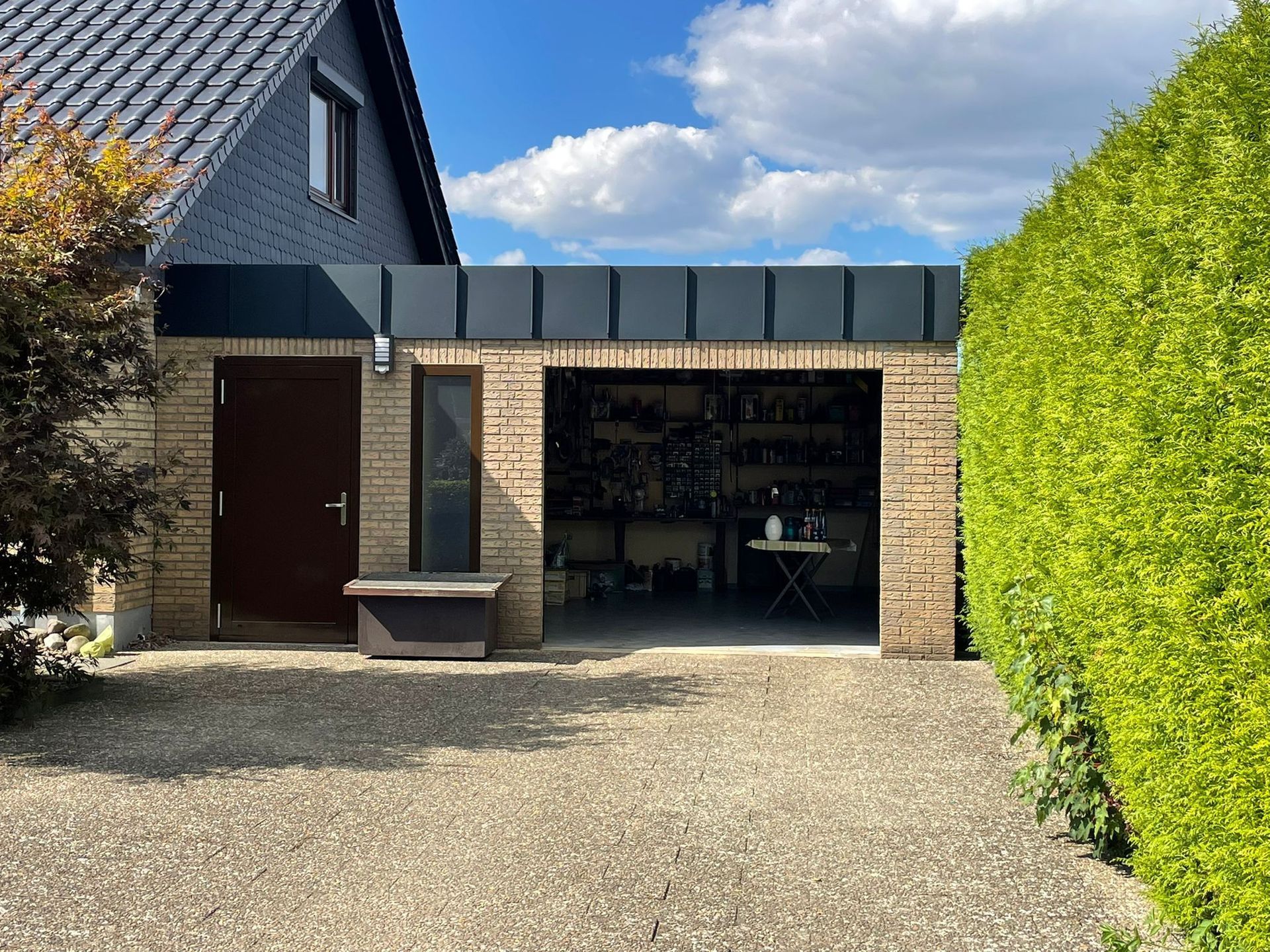Neben einem Haus steht eine Garage mit schwarzem Dach.