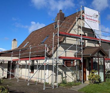 Ein Haus mit einem Gerüst darum und einem Schild mit der Aufschrift „Dachdecker“ darauf.