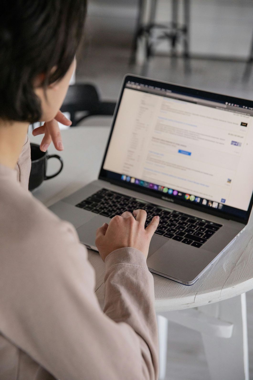 Person, die drinnen an einem weißen Tisch an einem Laptop arbeitet und auf der Tastatur tippt.