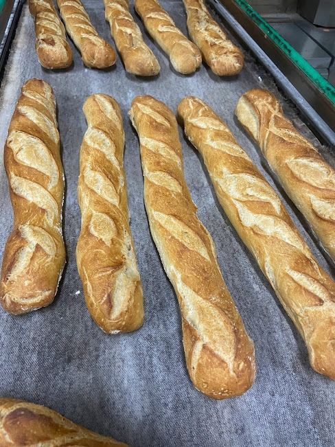 Baguettes de color marrón dorado con cortes diagonales, dispuestas en filas sobre una bandeja forrada con papel pergamino.