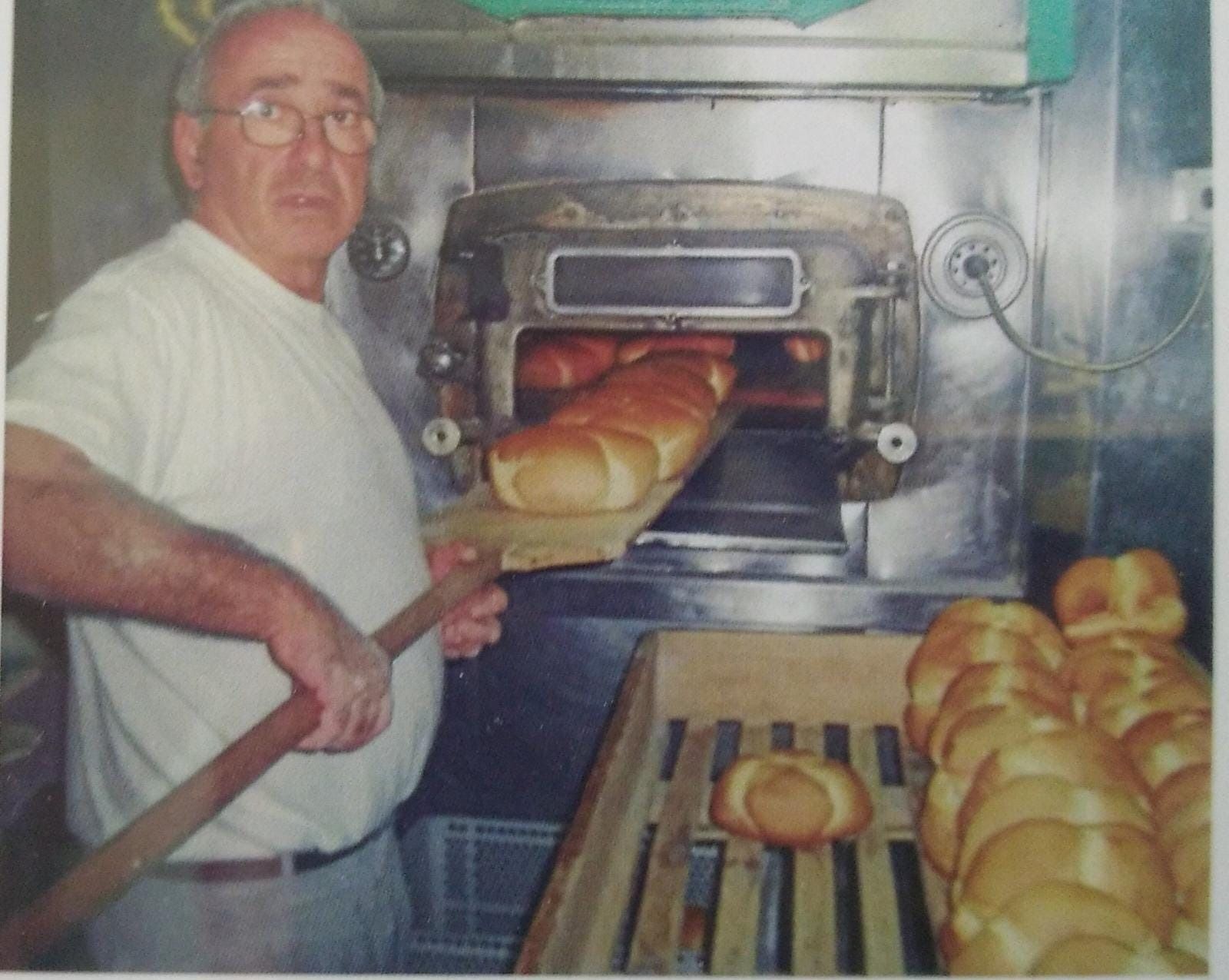 Una persona utiliza una pala de madera para sacar panes dorados de un gran horno industrial en una panadería.