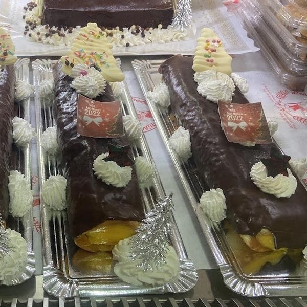 Tres troncos de Navidad de chocolate decorados con crema batida blanca, caramelos y pequeños adornos sobre bandejas de plata.
