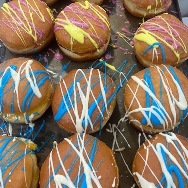 Una colección de rosquillas redondas fritas en una bandeja, decoradas con chorritos de glaseado amarillo, rosa, azul y blanco.