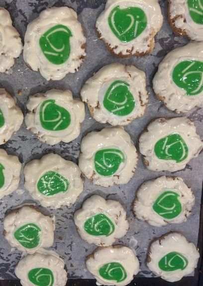 Una tanda de galletas redondas con glaseado blanco sobre papel pergamino, cada una coronada con un remolino verde vibrante en el centro.