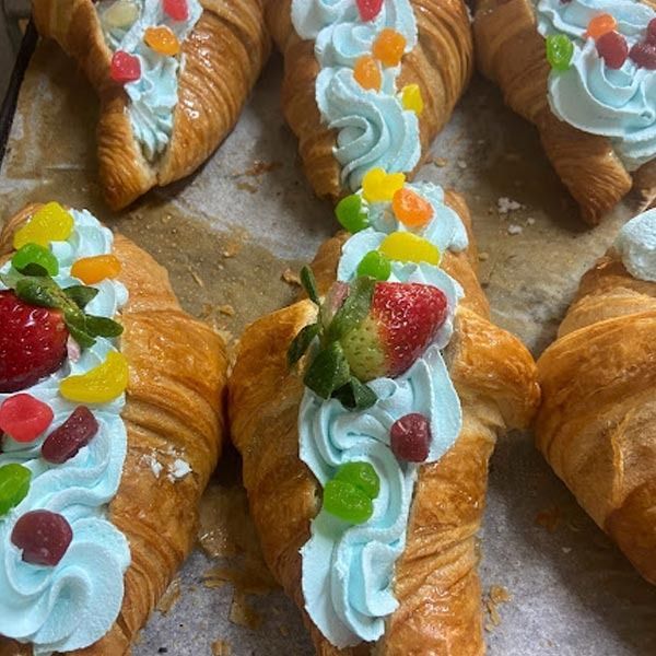 Croissants recién hechos rellenos de crema batida azul claro, cubiertos con fresas frescas y caramelos de goma de colores variados.