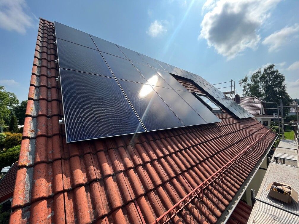 Auf einem roten Ziegeldach wurden Solarpaneele unter strahlendem Sonnenlicht installiert.
