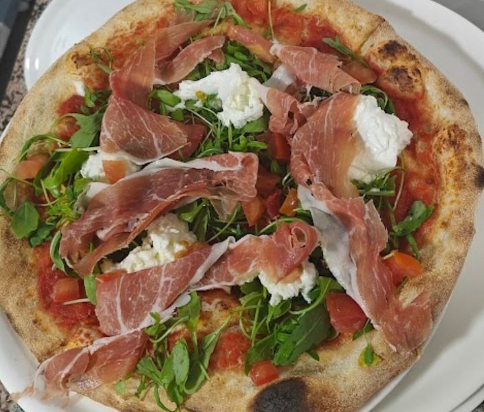 Pizza con prosciutto, rúcula y mozzarella en un plato blanco.