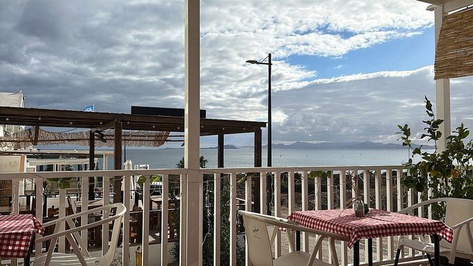 Terraza del restaurante con vistas al océano, manteles a cuadros y cielo nublado.