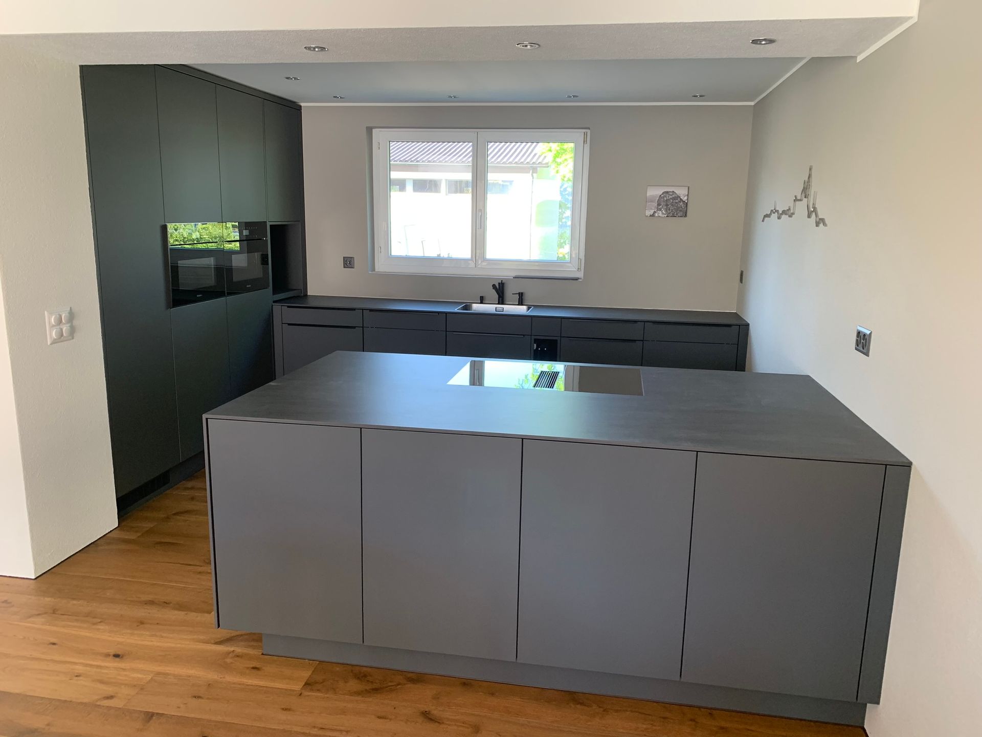 Eine moderne Küche mit einer dunkelgrauen Kücheninsel und passenden Schränken vor einer hellen Wand und Holzboden.