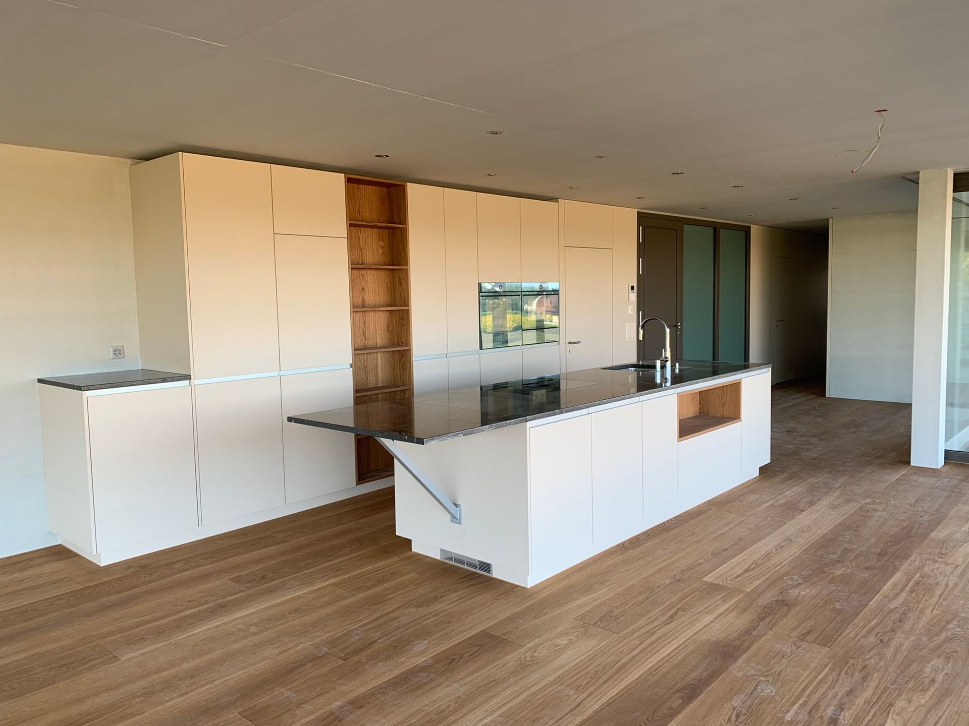 Eine moderne, minimalistische Küche mit weissen Schränken, einer grossen Kochinsel mit schwarzer Arbeitsplatte und Naturholzboden.