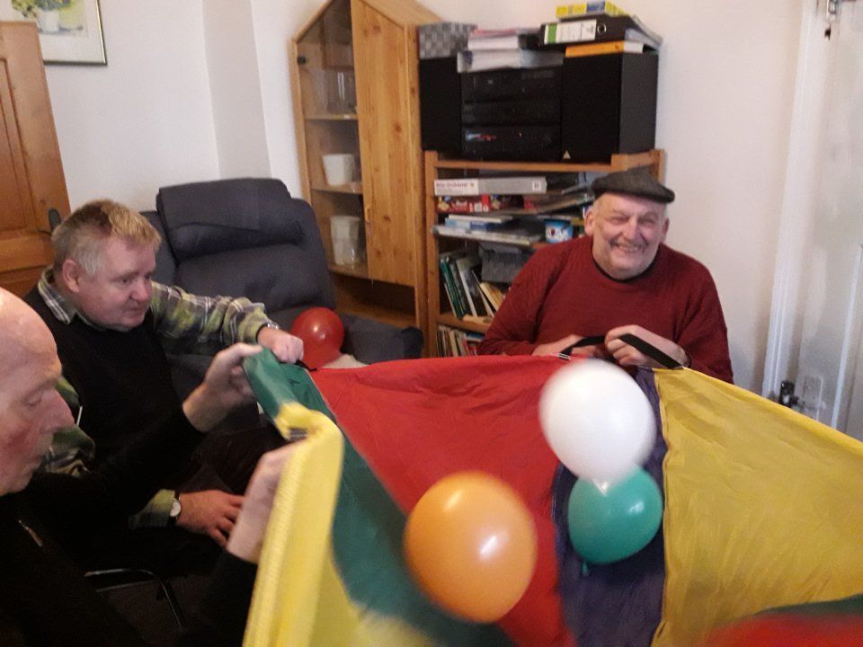 Drei Senioren spielen ein Spiel mit einer bunten Decke und Luftballons