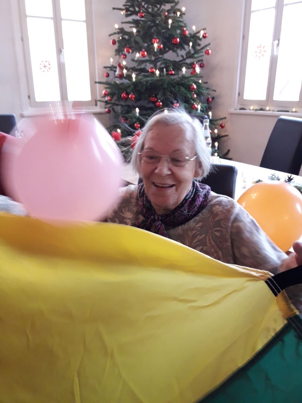 Seniorin sitzt mit dem Rücken zum Weihnachtsbaum, um sie Luftballons