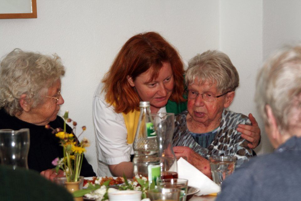 Pflegerin beugt sich hinunter zu Seniorin am gedeckten Tisch