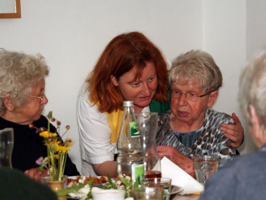 Pflegerin beugt sich hinunter zu Seniorin am gedeckten Tisch