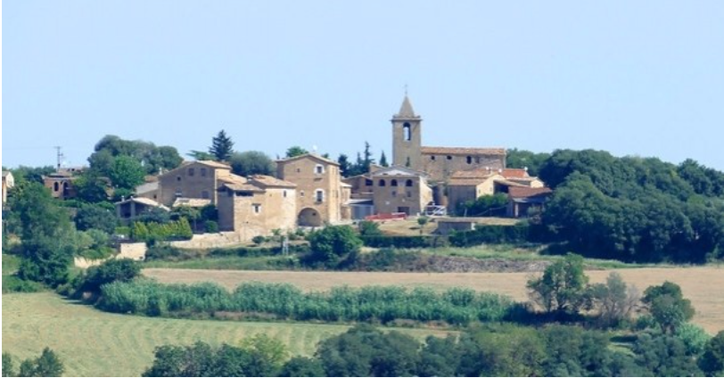 Un petit poble està situat al cim d'un turó envoltat d'arbres i camps.