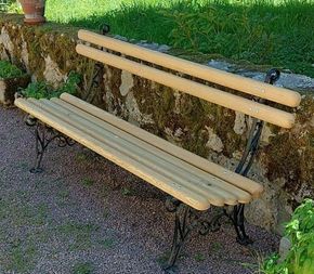 Un banc de jardin aux lattes de bois clair et aux pieds en fer noir ouvragés, placé devant un mur de pierre