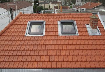 Un toit en tuiles de terre cuite avec deux puits de lumière et une cheminée en briques