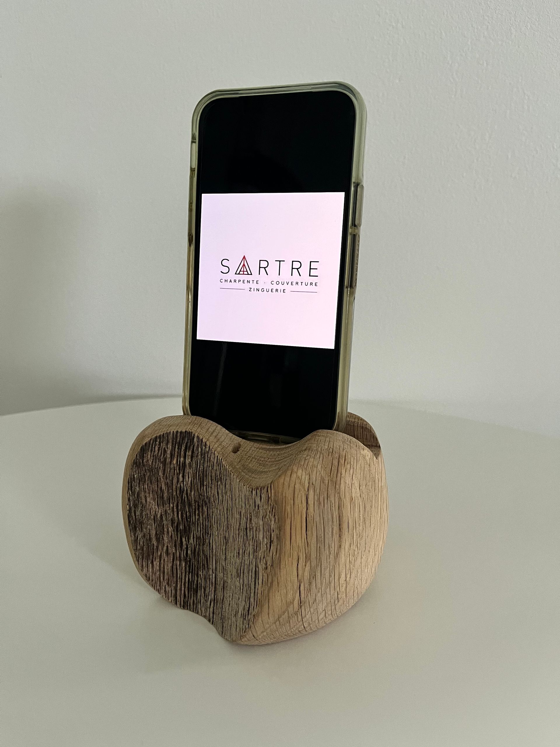 Un smartphone repose debout dans un petit support sculpté dans un morceau de bois