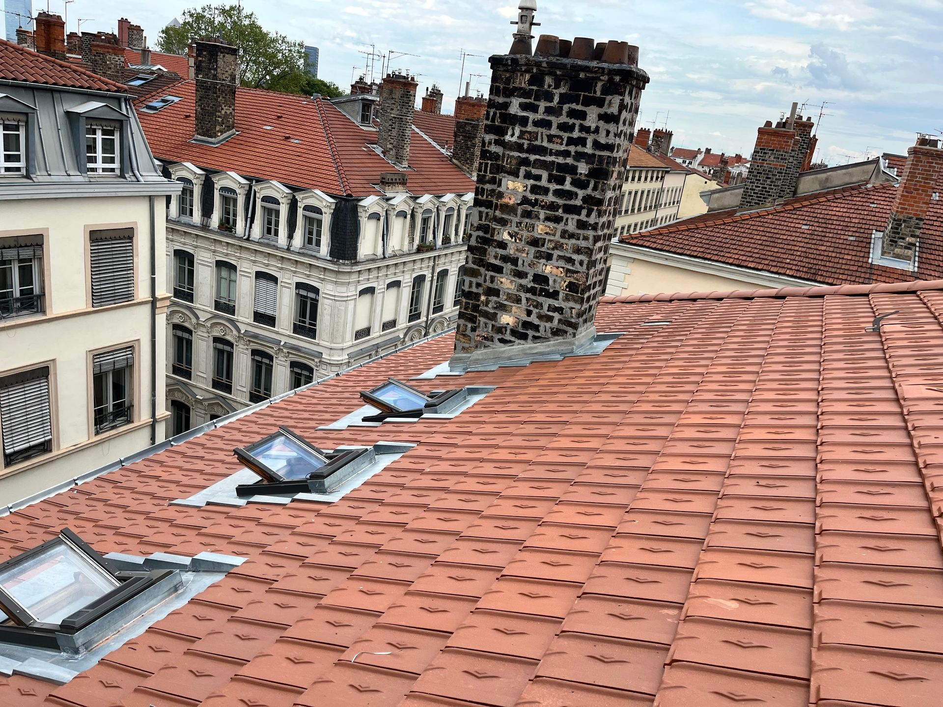 Un toit avec trois fenêtres de toit, une grande cheminée en briques et une vue sur des bâtiments historiques de style européen au loin