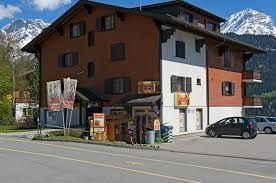 Un grand bâtiment avec des voitures garées devant et des montagnes en arrière-plan.