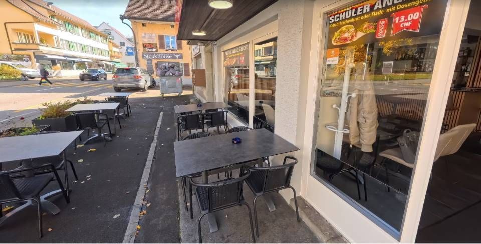 Außenansicht eines Restaurants mit Außensitzplätzen. Tische und Stühle auf dem Bürgersteig. Im Schaufenster ist die Speisekarte ausgestellt.