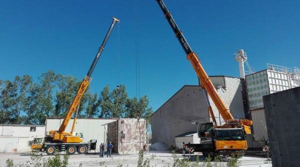 Dos grúas amarillas levantando vigas en una obra de construcción bajo un cielo azul despejado.