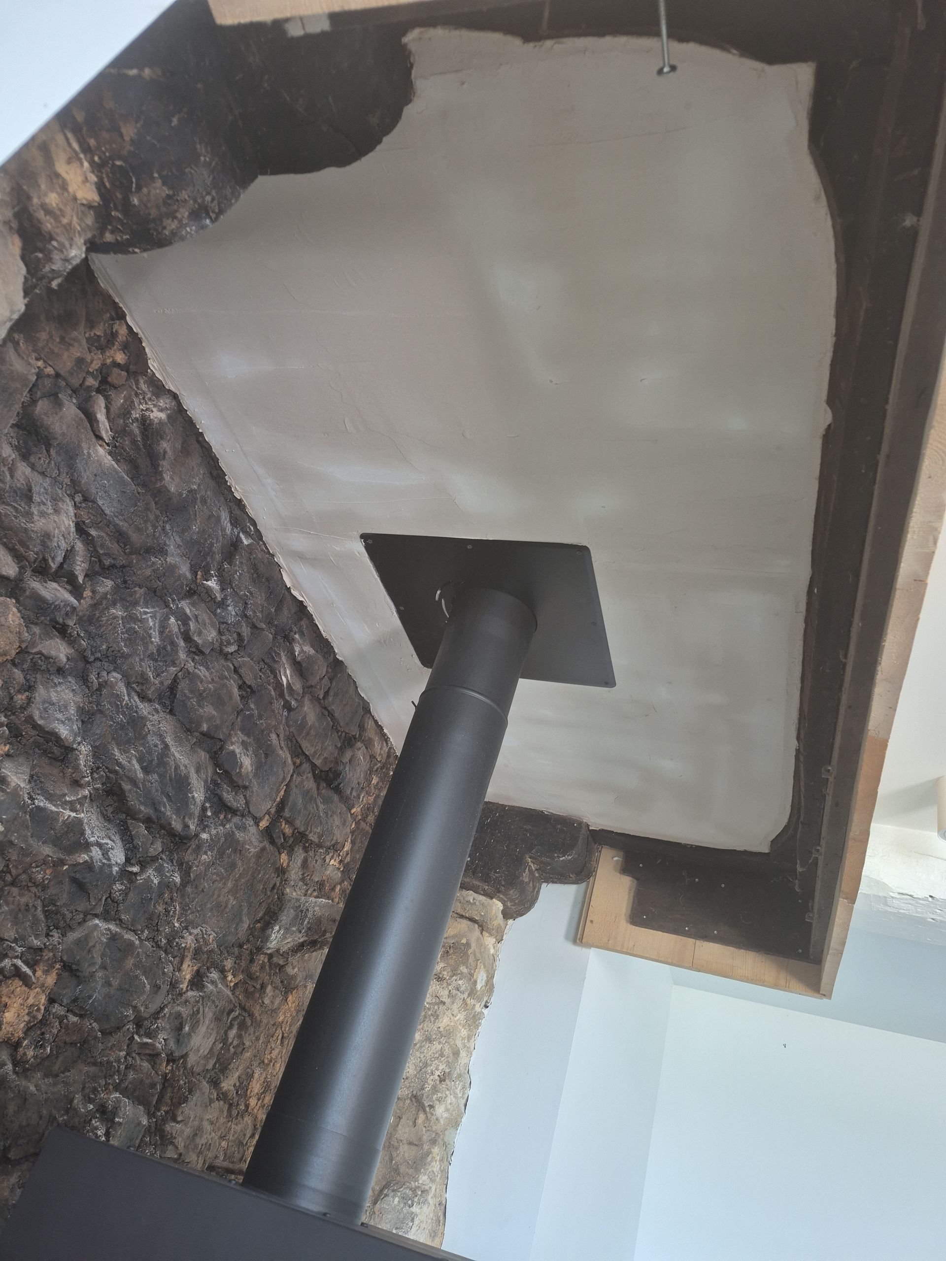 Tuyau de poêle noir traversant un plafond. Ce plafond est recouvert d'un revêtement ignifuge blanc et irrégulier.