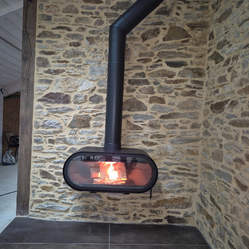 Une cheminée noire moderne est accrochée à un mur de pierre rustique, les flammes étant visibles à travers le verre.