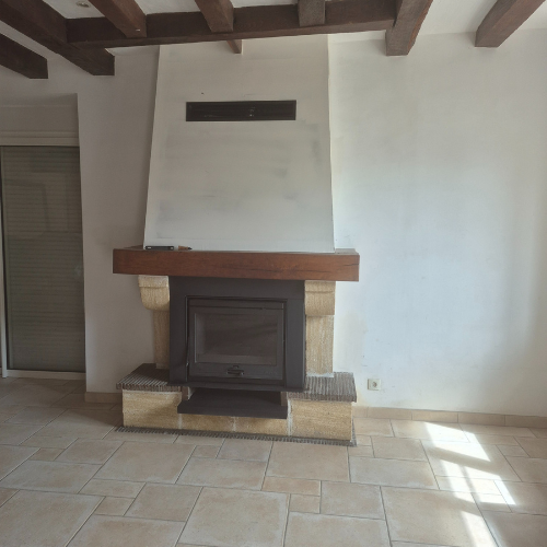 Cheminée dans une pièce avec sol en carrelage de pierre, poutres en bois et porte fermée.