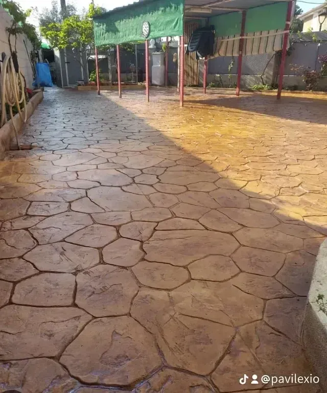 Hormigón estampado de color marrón claro con textura y un patrón irregular que imita la piedra, bordeado por un bordillo pintado.