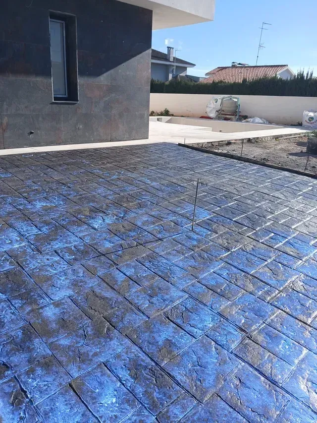 Un camino pavimentado serpenteaba hacia un jardín exuberante y bien cuidado, con plantas decorativas e iluminación tenue a ras de suelo al anochecer.