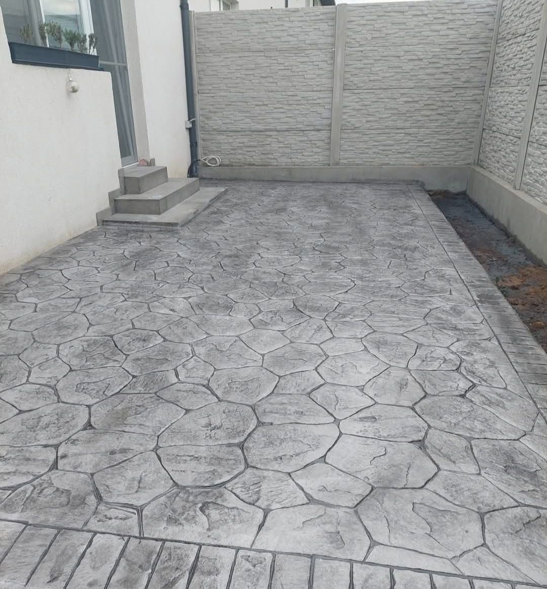 Entrada de hormigón con diseño de piedra que conduce a una puerta cerrada junto a la pared de la casa.