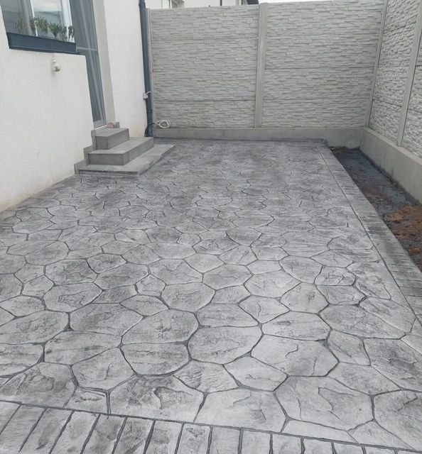 Entrada de hormigón junto a un muro blanco, con verja y un pequeño rellano con escalones.