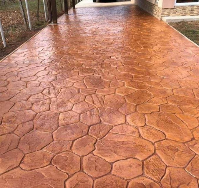 Pasarela de hormigón estampado de color marrón rojizo texturizado bajo un área exterior cubierta.