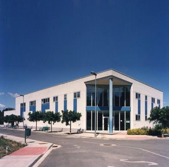 Un gran edificio blanco con detalles azules está rodeado de árboles.
