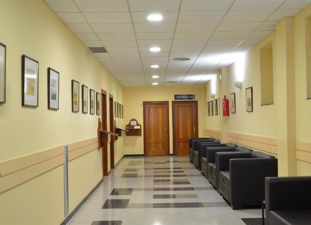 Un largo pasillo con sillas y un extintor en la pared.