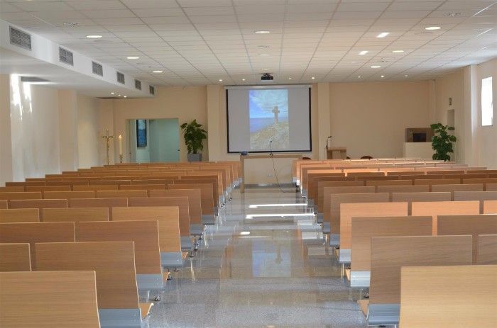 Una sala grande con filas de bancos de madera y una pantalla de proyección.